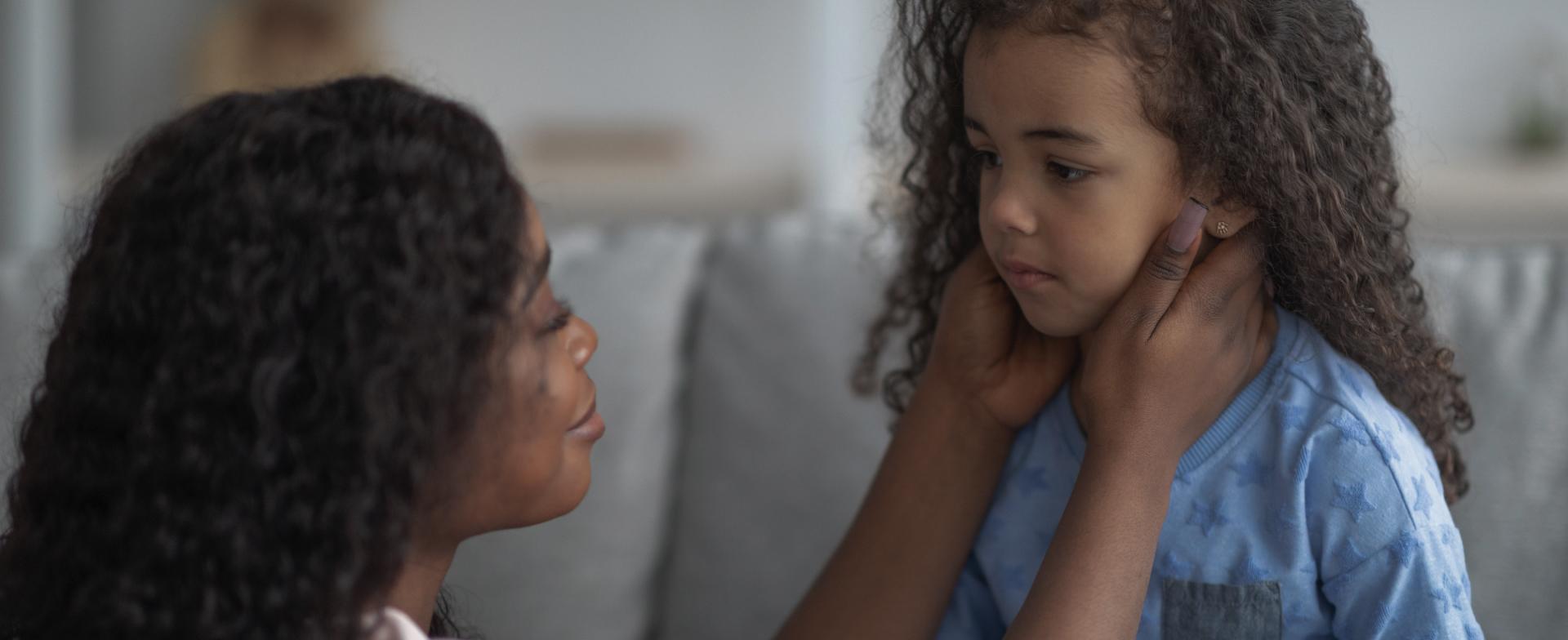 Moeder en dochter Een mama die haar handen op haar dochter haar kaken legt om haar te troosten.